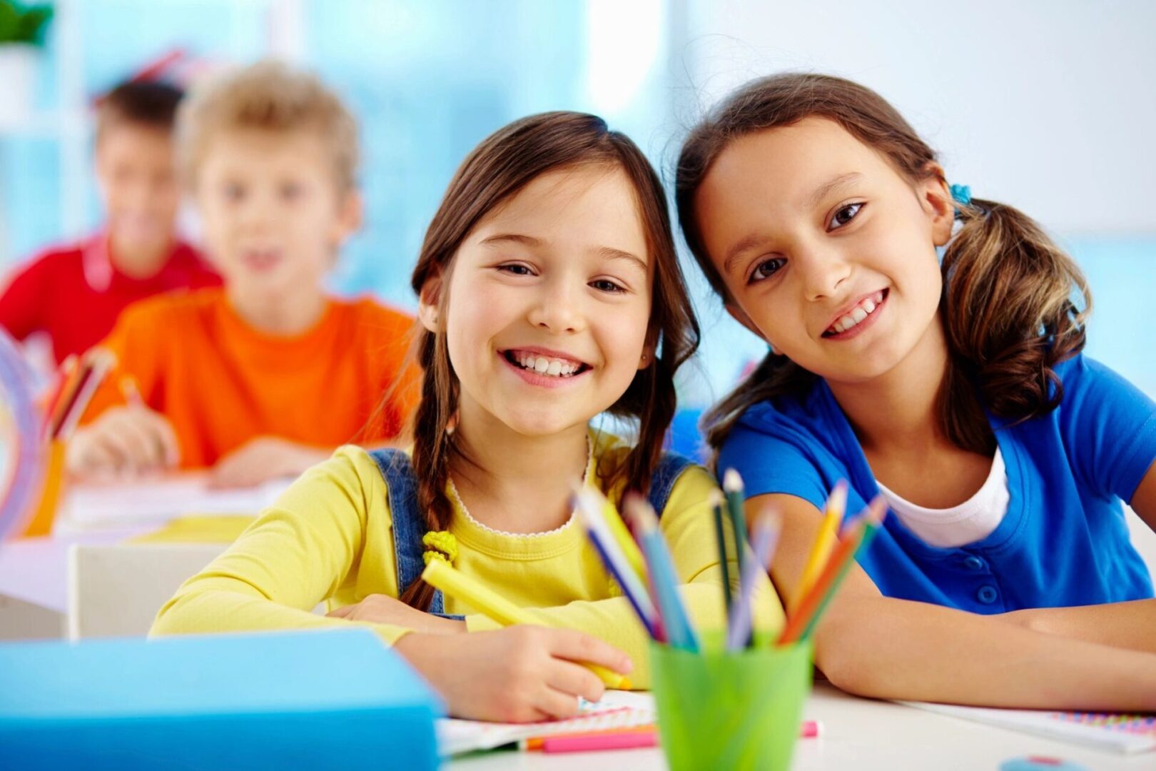 Two children smile while sitting at a table.