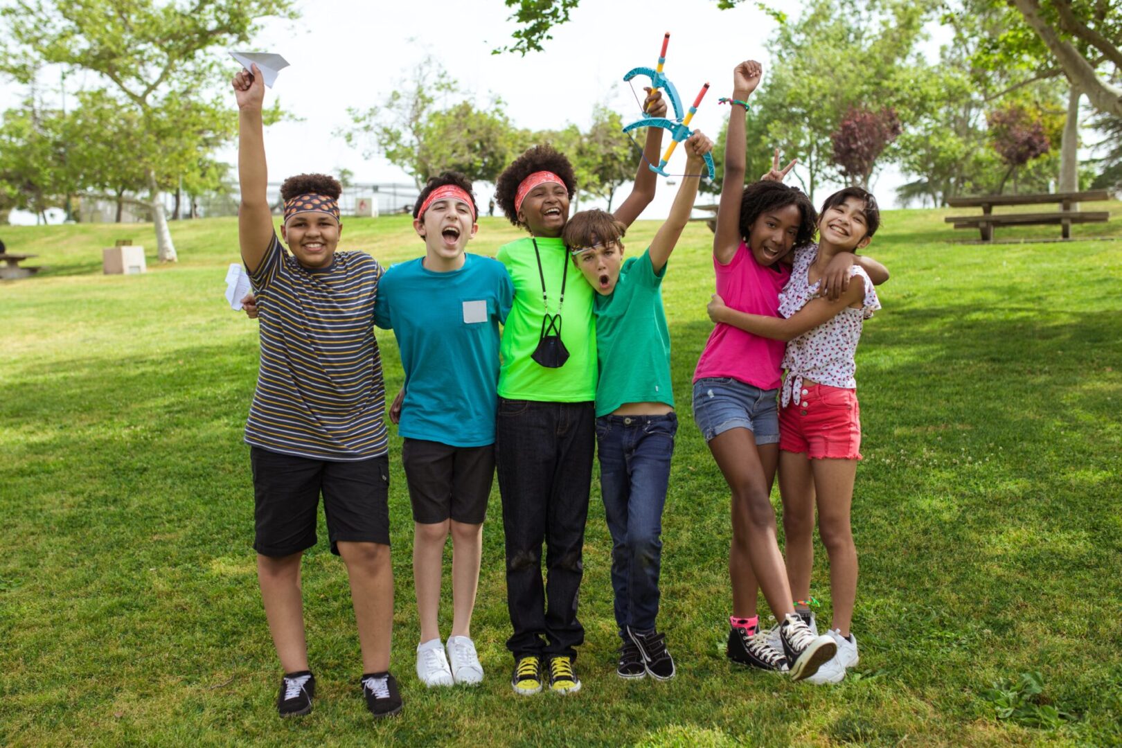 A group of kids standing in the grass with their arms raised.